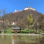 Výlet na hrad Bezděz: král hradů Máchova kraje s nejkrásnějšími výhledy v severních Čechách Hrad Bezděz patří mezi nejpůsobivější gotické hrady v České republice. Tyčí se na výrazném čedičovém vrchu nad krajinou Máchova kraje a už z dálky působí majestátně a tajemně. Díky své zachovalosti, dramatické poloze i bohaté historii je ideálním cílem pro rodiny s dětmi, turisty, cyklisty i milovníky romantických výhledů. Výstup na hrad je sice místy náročnější, ale odměnou je jeden z nejkrásnějších panoramatických rozhledů v severních Čechách. Historie hradu Bezděz: královská pevnost i vězení mladého panovníka Hrad Bezděz založil roku 1264 král Přemysl Otakar II. jako strategickou královskou pevnost chránící obchodní stezky i severní hranici českého království. Díky své poloze patřil mezi nejdůležitější obranné body tehdejší země. Jednou z nejznámějších událostí spojených s hradem je věznění mladého krále Václava II. v roce 1279. Po smrti Přemysla Otakara II. v bitvě na Moravském poli byl malý následník trůnu spolu se svou matkou Kunhutou internován na příkaz Oty Braniborského právě zde. Tato dramatická kapitola dodává hradu dodnes silnou historickou atmosféru. Později hrad přešel do rukou šlechty, krátce jej ovládli husité a postupně byl opuštěn. Díky tomu se však dochoval v mimořádně autentické gotické podobě. Co dnes uvidíte na hradě Bezděz Dnešní podoba hradu patří mezi nejzachovalejší gotické hradní komplexy v Česku. Při návštěvě si projdete několik nádvoří, paláce i dominantní věž. Největší zajímavosti hradu: Velká věž (34 metrů) – nabízí jedinečný kruhový výhled na Máchovo jezero, Ralsko, Ještěd i Krkonoše Kaple sv. Michaela – mimořádně zachovalá gotická kaple s křížovou klenbou Královský palác – připomínka pobytu Václava II. hradní expozice – historie hradu a jeho legendy druhé nádvoří – atmosférické místo s výhledy do krajiny Bezděz je právem označován jako král hradů severních Čech. Turistické trasy na hrad Bezděz Nejkratší cesta z obce Bezděz (červená značka) délka: 1,8 km náročnost: střední vhodná pro rodiny se staršími dětmi Nejoblíbenější výstup vede lesní cestou přímo od parkoviště v obci Bezděz. Poslední úsek je prudší a kamenitý, ale zvládne jej většina návštěvníků. Trasa z Doks kolem Máchova jezera délka: 8 km náročnost: střední Krásná cesta spojuje koupání u Máchova jezera s výstupem na hrad. Ideální varianta pro celodenní výlet. Ze Starých Splavů přes Doksy délka: 10 km náročnost: střední Trasa vede lesy i rekreační oblastí kolem jezera a nabízí příjemnou kombinaci přírody a výhledů. Z Bělé pod Bezdězem délka: 12 km náročnost: středně náročná Delší turistická varianta vhodná pro zkušenější výletníky. Cyklotrasy v okolí hradu Bezděz Okolí Bezdězu je ideální i pro cyklistiku. Cyklotrasa 3045 Doksy – Bezděz – Ralsko 25 km, střední náročnost Cyklotrasa 241 Mladá Boleslav – Bezděz – Česká Lípa 50 km, náročnější trasa Okruh kolem Bezdězu Bezděz – Houska – Máchovo jezero – Bezděz cca 25 km, ideální jednodenní výlet Jak se dostat na hrad Bezděz Autem Parkování je možné přímo v obci Bezděz. Odtud pokračujete pěšky asi 30–40 minut. Vlakem Stanice Bezděz leží přibližně 3 km od hradu. Spojení vede například z Turnova, Bakova nad Jizerou nebo Doks. Autobusem Autobusová zastávka Bezděz obec je nejbližším výchozím bodem výstupu. Tipy na výlety v okolí hradu Bezděz Máchovo jezero Jedna z nejkrásnějších rekreačních oblastí severních Čech nabízí koupání, pláže, lodní dopravu i cyklostezky. Oblíbená je zejména trasa kolem jezera vedoucí přes Staré Splavy, Doksy a Borný. V létě jde o ideální kombinaci turistiky a relaxace u vody. Hrad Houska Tajemný hrad Houska patří mezi nejzáhadnější místa České republiky. Podle legend stojí nad průrvou vedoucí do podsvětí. Návštěvníky zde čekají historické interiéry, fresky i silná atmosféra. Hrad leží asi 15 km od Bezdězu a je skvělým doplňkem výletu. Skalní hrad Sloup v Čechách Unikátní skalní hrad vytesaný do pískovcové skály nabízí romantickou procházku i krásné výhledy do krajiny Lužických hor. Výstup po schodištích ve skále patří mezi nejzajímavější zážitky regionu. Vrátenská hora a rozhledna Rozhledna na Vrátenské hoře nabízí jeden z nejhezčích panoramatických výhledů v oblasti Kokořínska. Za dobré viditelnosti lze spatřit Krkonoše i České středohoří. Bělá pod Bezdězem Historické město s renesanční radnicí, zachovalým náměstím a klidnou atmosférou je ideální zastávkou před nebo po výstupu na hrad. Praktické informace pro návštěvníky poloha: Liberecký kraj, Máchův kraj přístup: pěšky z obce Bezděz vhodné pro děti: ano (poslední úsek prudší) vhodné pro kočárky: ne vhodné pro kola: pouze pod hrad nejlepší období návštěvy: jaro, podzim, léto délka výstupu: cca 30–45 minut Proč navštívit hrad Bezděz Bezděz patří mezi nejromantičtější hrady České republiky. Nabízí jedinečné výhledy, autentickou gotickou architekturu i silné historické příběhy. Spojení výstupu na hrad s návštěvou Máchova jezera, hradu Houska nebo skalního hradu Sloup vytvoří perfektní celodenní program pro rodiny i aktivní turisty. Pokud hledáte výlet, který spojuje historii, přírodu a nezapomenutelné panoramatické výhledy, hrad Bezděz vás rozhodně nezklame.