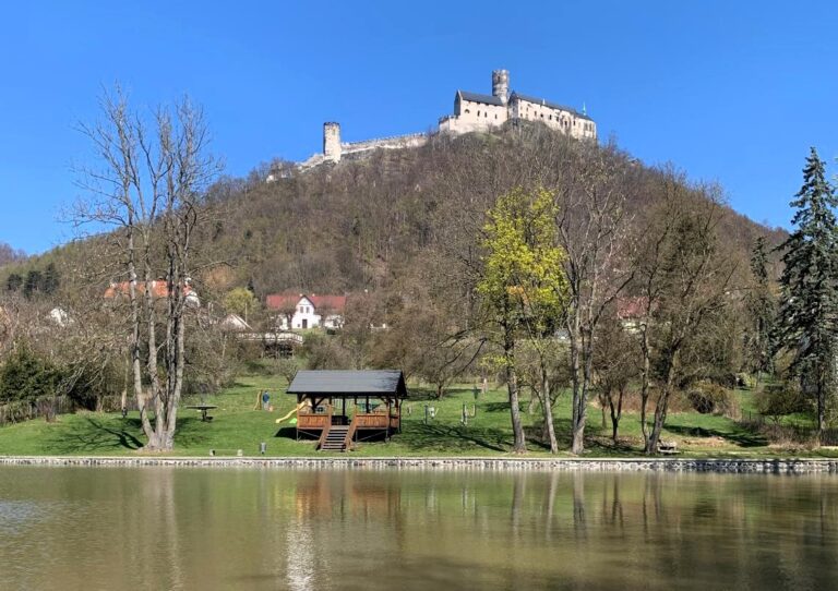Výlet na hrad Bezděz: král hradů Máchova kraje s nejkrásnějšími výhledy v severních Čechách Hrad Bezděz patří mezi nejpůsobivější gotické hrady v České republice. Tyčí se na výrazném čedičovém vrchu nad krajinou Máchova kraje a už z dálky působí majestátně a tajemně. Díky své zachovalosti, dramatické poloze i bohaté historii je ideálním cílem pro rodiny s dětmi, turisty, cyklisty i milovníky romantických výhledů. Výstup na hrad je sice místy náročnější, ale odměnou je jeden z nejkrásnějších panoramatických rozhledů v severních Čechách. Historie hradu Bezděz: královská pevnost i vězení mladého panovníka Hrad Bezděz založil roku 1264 král Přemysl Otakar II. jako strategickou královskou pevnost chránící obchodní stezky i severní hranici českého království. Díky své poloze patřil mezi nejdůležitější obranné body tehdejší země. Jednou z nejznámějších událostí spojených s hradem je věznění mladého krále Václava II. v roce 1279. Po smrti Přemysla Otakara II. v bitvě na Moravském poli byl malý následník trůnu spolu se svou matkou Kunhutou internován na příkaz Oty Braniborského právě zde. Tato dramatická kapitola dodává hradu dodnes silnou historickou atmosféru. Později hrad přešel do rukou šlechty, krátce jej ovládli husité a postupně byl opuštěn. Díky tomu se však dochoval v mimořádně autentické gotické podobě. Co dnes uvidíte na hradě Bezděz Dnešní podoba hradu patří mezi nejzachovalejší gotické hradní komplexy v Česku. Při návštěvě si projdete několik nádvoří, paláce i dominantní věž. Největší zajímavosti hradu: Velká věž (34 metrů) – nabízí jedinečný kruhový výhled na Máchovo jezero, Ralsko, Ještěd i Krkonoše Kaple sv. Michaela – mimořádně zachovalá gotická kaple s křížovou klenbou Královský palác – připomínka pobytu Václava II. hradní expozice – historie hradu a jeho legendy druhé nádvoří – atmosférické místo s výhledy do krajiny Bezděz je právem označován jako král hradů severních Čech. Turistické trasy na hrad Bezděz Nejkratší cesta z obce Bezděz (červená značka) délka: 1,8 km náročnost: střední vhodná pro rodiny se staršími dětmi Nejoblíbenější výstup vede lesní cestou přímo od parkoviště v obci Bezděz. Poslední úsek je prudší a kamenitý, ale zvládne jej většina návštěvníků. Trasa z Doks kolem Máchova jezera délka: 8 km náročnost: střední Krásná cesta spojuje koupání u Máchova jezera s výstupem na hrad. Ideální varianta pro celodenní výlet. Ze Starých Splavů přes Doksy délka: 10 km náročnost: střední Trasa vede lesy i rekreační oblastí kolem jezera a nabízí příjemnou kombinaci přírody a výhledů. Z Bělé pod Bezdězem délka: 12 km náročnost: středně náročná Delší turistická varianta vhodná pro zkušenější výletníky. Cyklotrasy v okolí hradu Bezděz Okolí Bezdězu je ideální i pro cyklistiku. Cyklotrasa 3045 Doksy – Bezděz – Ralsko 25 km, střední náročnost Cyklotrasa 241 Mladá Boleslav – Bezděz – Česká Lípa 50 km, náročnější trasa Okruh kolem Bezdězu Bezděz – Houska – Máchovo jezero – Bezděz cca 25 km, ideální jednodenní výlet Jak se dostat na hrad Bezděz Autem Parkování je možné přímo v obci Bezděz. Odtud pokračujete pěšky asi 30–40 minut. Vlakem Stanice Bezděz leží přibližně 3 km od hradu. Spojení vede například z Turnova, Bakova nad Jizerou nebo Doks. Autobusem Autobusová zastávka Bezděz obec je nejbližším výchozím bodem výstupu. Tipy na výlety v okolí hradu Bezděz Máchovo jezero Jedna z nejkrásnějších rekreačních oblastí severních Čech nabízí koupání, pláže, lodní dopravu i cyklostezky. Oblíbená je zejména trasa kolem jezera vedoucí přes Staré Splavy, Doksy a Borný. V létě jde o ideální kombinaci turistiky a relaxace u vody. Hrad Houska Tajemný hrad Houska patří mezi nejzáhadnější místa České republiky. Podle legend stojí nad průrvou vedoucí do podsvětí. Návštěvníky zde čekají historické interiéry, fresky i silná atmosféra. Hrad leží asi 15 km od Bezdězu a je skvělým doplňkem výletu. Skalní hrad Sloup v Čechách Unikátní skalní hrad vytesaný do pískovcové skály nabízí romantickou procházku i krásné výhledy do krajiny Lužických hor. Výstup po schodištích ve skále patří mezi nejzajímavější zážitky regionu. Vrátenská hora a rozhledna Rozhledna na Vrátenské hoře nabízí jeden z nejhezčích panoramatických výhledů v oblasti Kokořínska. Za dobré viditelnosti lze spatřit Krkonoše i České středohoří. Bělá pod Bezdězem Historické město s renesanční radnicí, zachovalým náměstím a klidnou atmosférou je ideální zastávkou před nebo po výstupu na hrad. Praktické informace pro návštěvníky poloha: Liberecký kraj, Máchův kraj přístup: pěšky z obce Bezděz vhodné pro děti: ano (poslední úsek prudší) vhodné pro kočárky: ne vhodné pro kola: pouze pod hrad nejlepší období návštěvy: jaro, podzim, léto délka výstupu: cca 30–45 minut Proč navštívit hrad Bezděz Bezděz patří mezi nejromantičtější hrady České republiky. Nabízí jedinečné výhledy, autentickou gotickou architekturu i silné historické příběhy. Spojení výstupu na hrad s návštěvou Máchova jezera, hradu Houska nebo skalního hradu Sloup vytvoří perfektní celodenní program pro rodiny i aktivní turisty. Pokud hledáte výlet, který spojuje historii, přírodu a nezapomenutelné panoramatické výhledy, hrad Bezděz vás rozhodně nezklame.